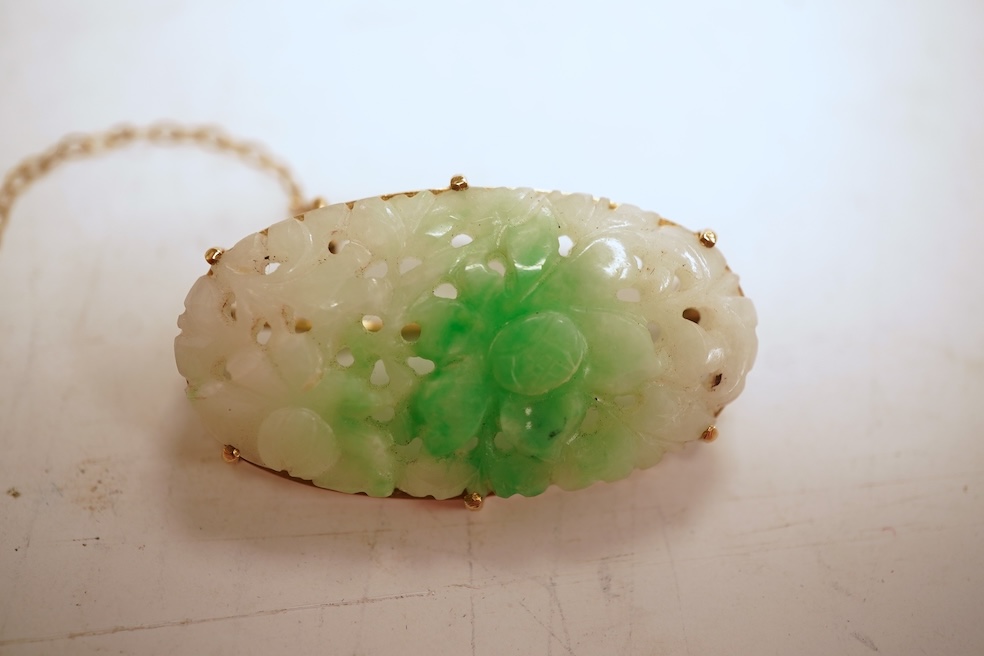 A jadeite brooch, set with an oval jadeite of mottled green and white, carved to depict flowers, mounted in 9ct gold, length 3.2cm, British hallmarks, maker's mark for Cropp & Farr, gross weight approximately 4.5 grams,